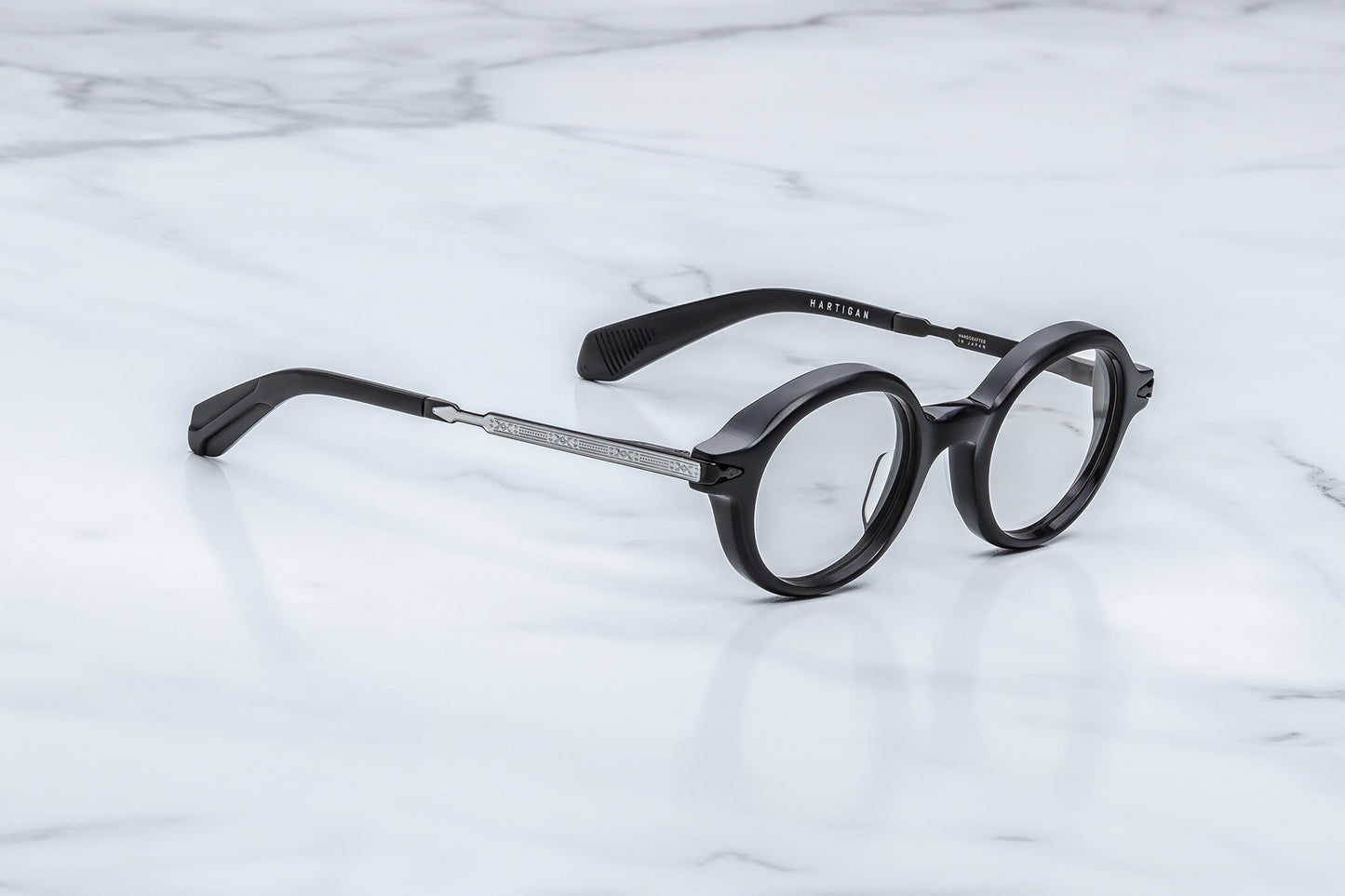 Round black eyeglasses with a silver metal bridge and temples, resting on a white marble surface.