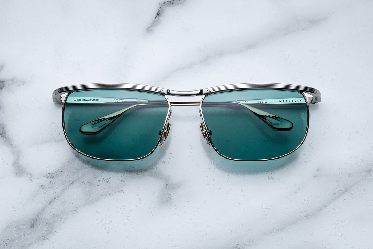 Overhead view of silver sunglasses with green lenses and gold accents