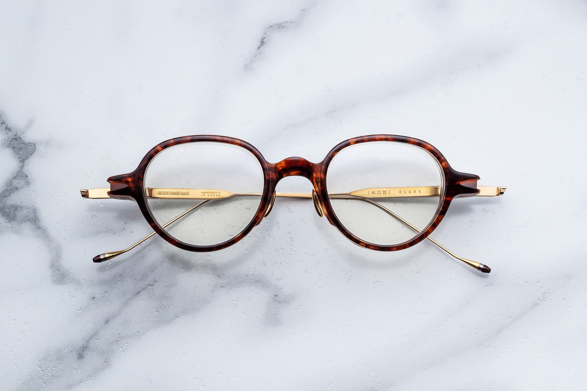 Round eyeglasses with a tortoiseshell acetate frame and gold metal temples, displayed flat on a white marble surface.