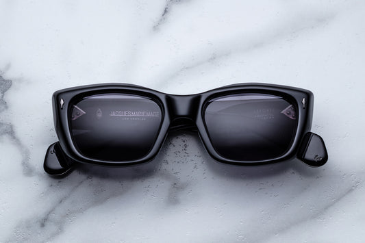 Black square sunglasses with dark lenses resting on a white marble surface.