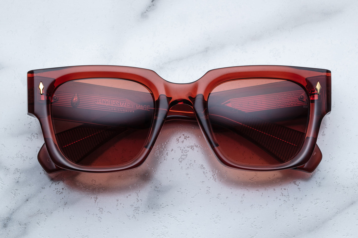 Overhead view of rectangular translucent red sunglasses with orange lenses and gold accents