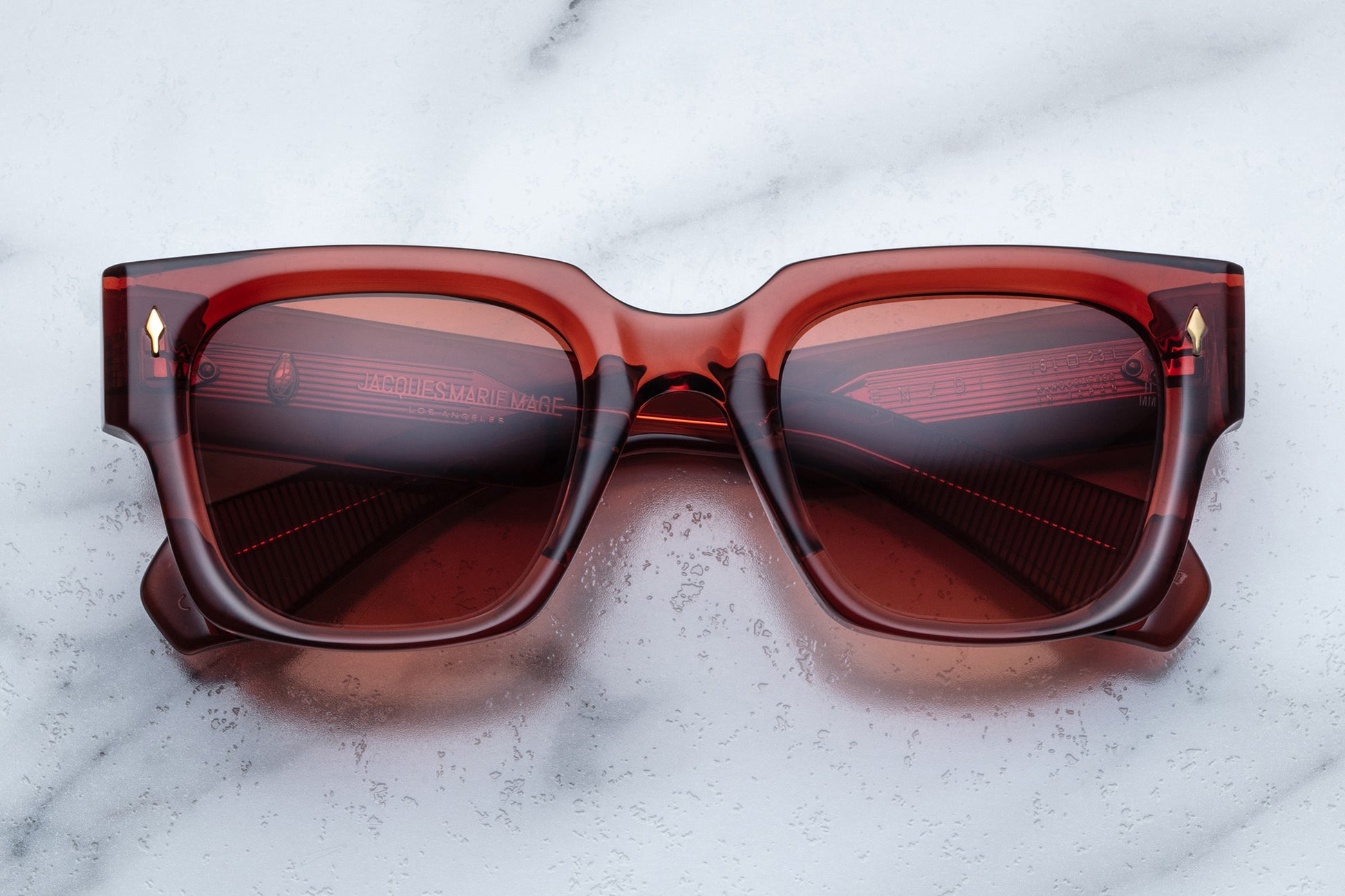Overhead view of rectangular translucent red sunglasses with orange lenses and gold accents