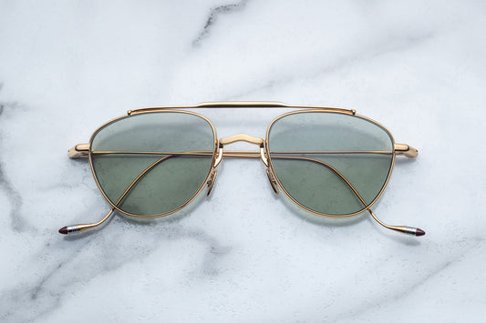 Overhead view of oval shaped sunglasses with bottle green lenses and a gold frame