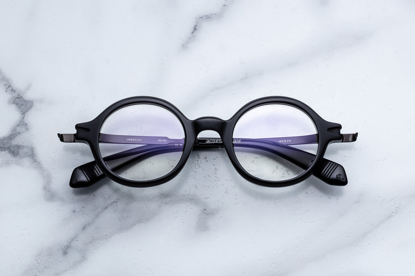 Round black eyeglass frames with purple temple arms, displayed on a white marble surface.