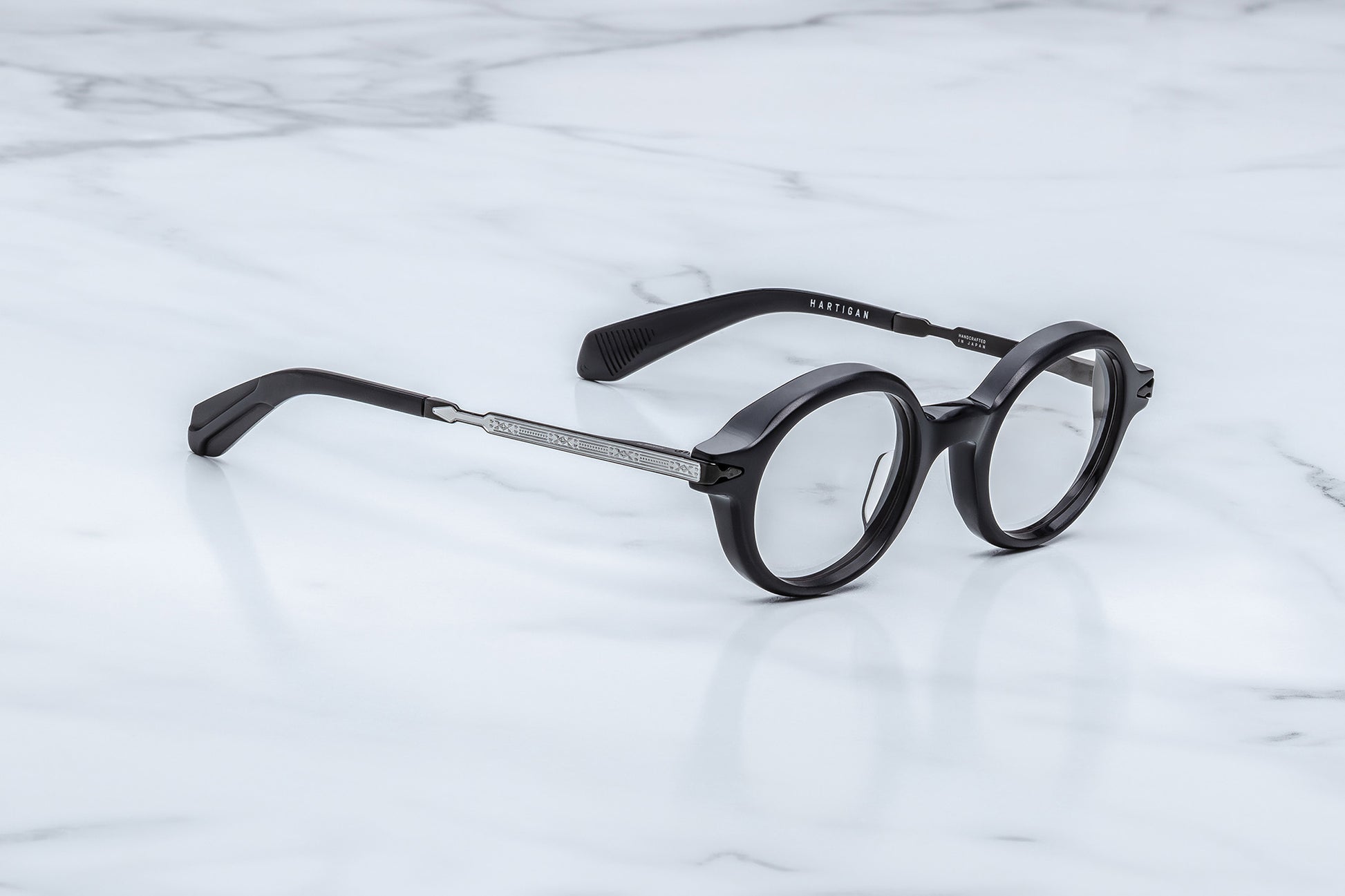 Round black eyeglasses with a silver metal bridge and temples, resting on a white marble surface.