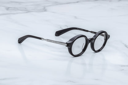 Round black eyeglasses with a silver metal bridge and temples, resting on a white marble surface.