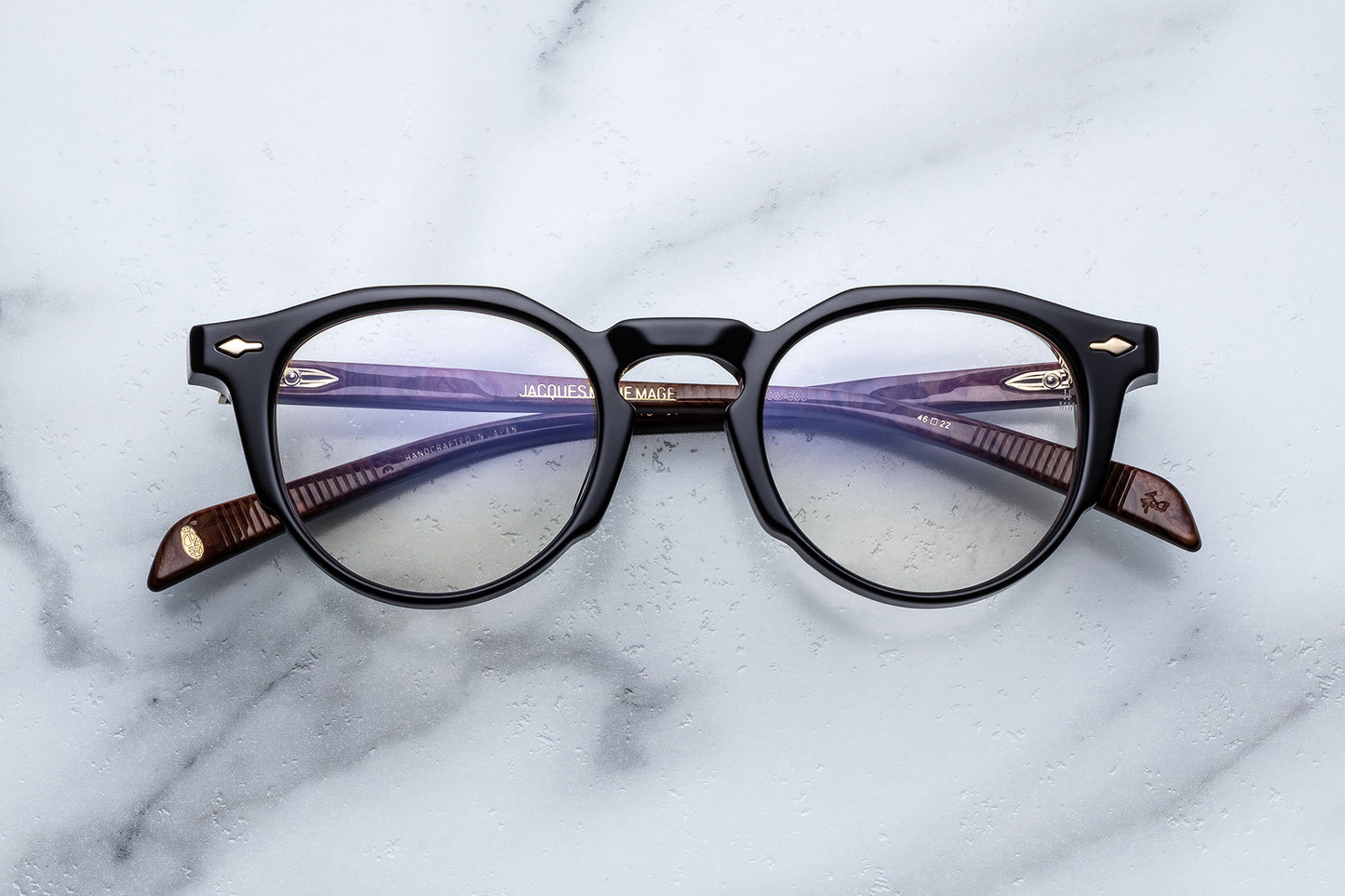 Round eyeglasses with black frame and gold accents on a marble surface