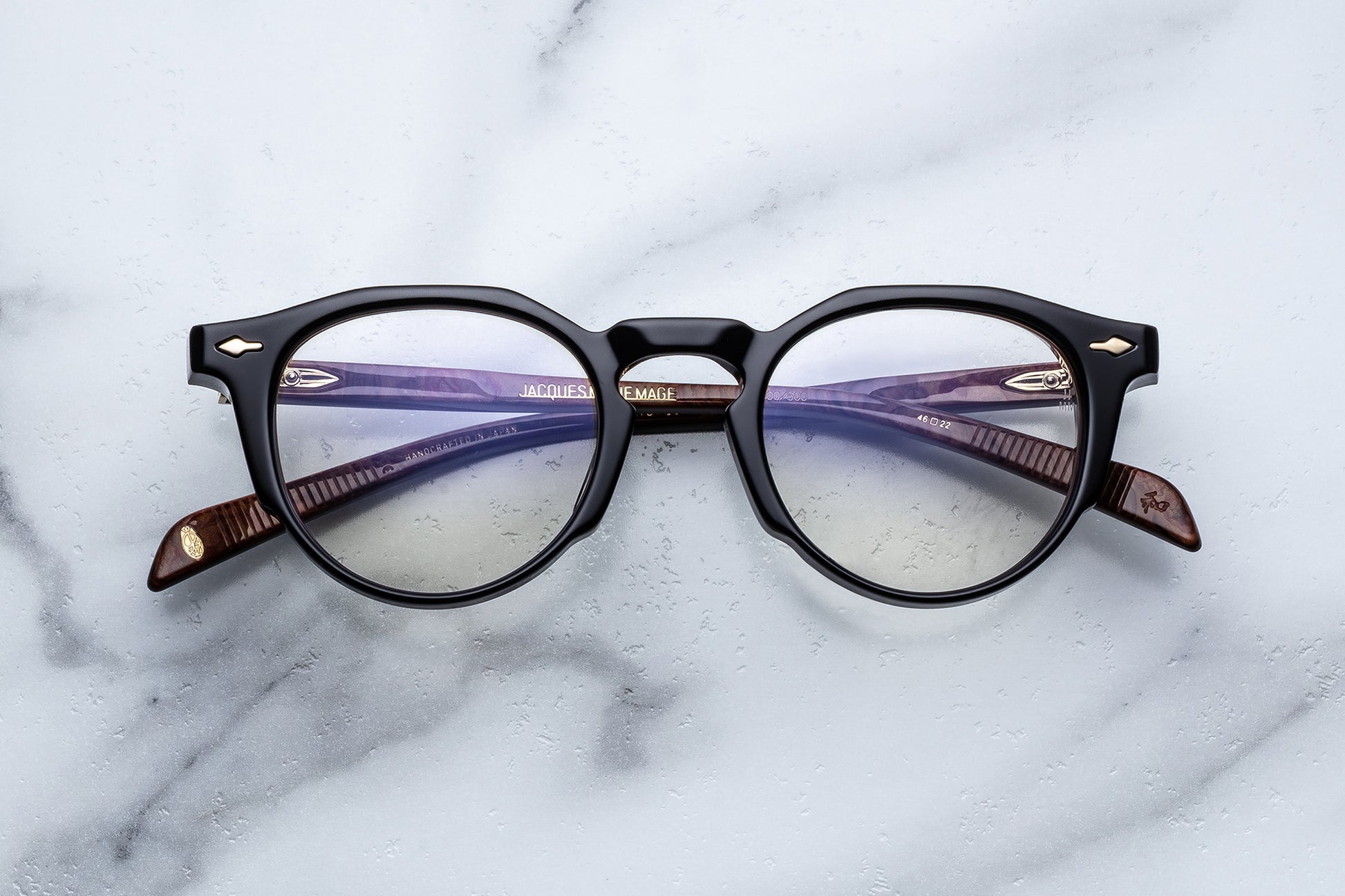 Round eyeglasses with black frame and gold accents on a marble surface