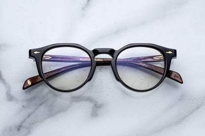 Round eyeglasses with black frame and gold accents on a marble surface
