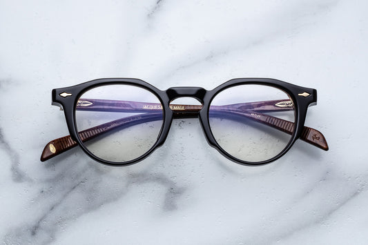 Round eyeglasses with black frame and gold accents on a marble surface