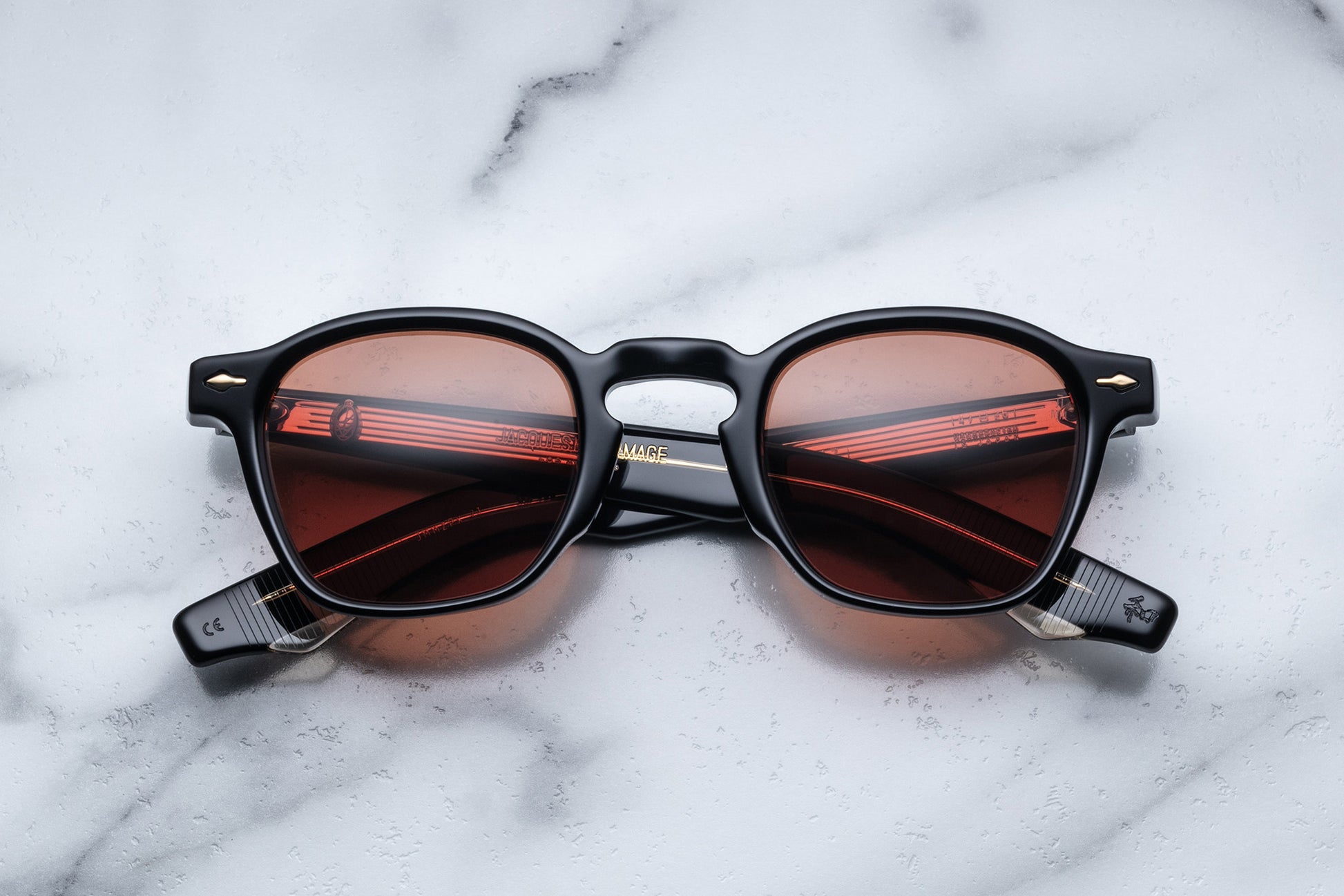 Overhead view of sunglasses with black frames and red-tinted lenses on a white marble surface
