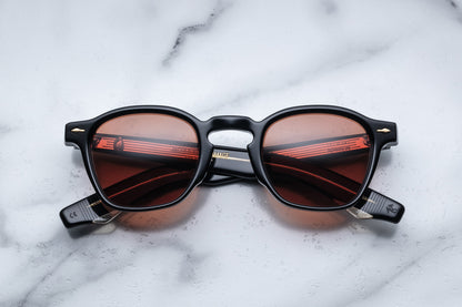 Overhead view of sunglasses with black frames and red-tinted lenses on a white marble surface
