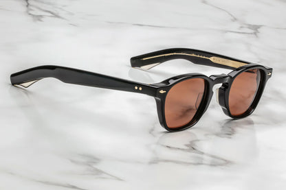 Profile view of sunglasses with black frames and red-tinted lenses on a white marble surface
